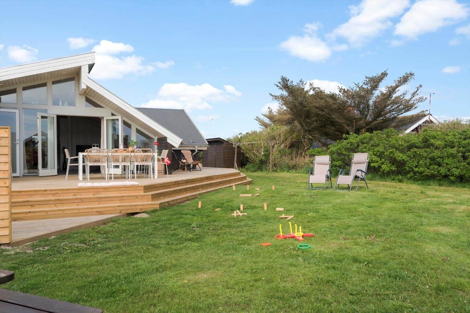Haus mit Terrasse, Garten und Liegestühlen. Spielzeug auf Rasen.