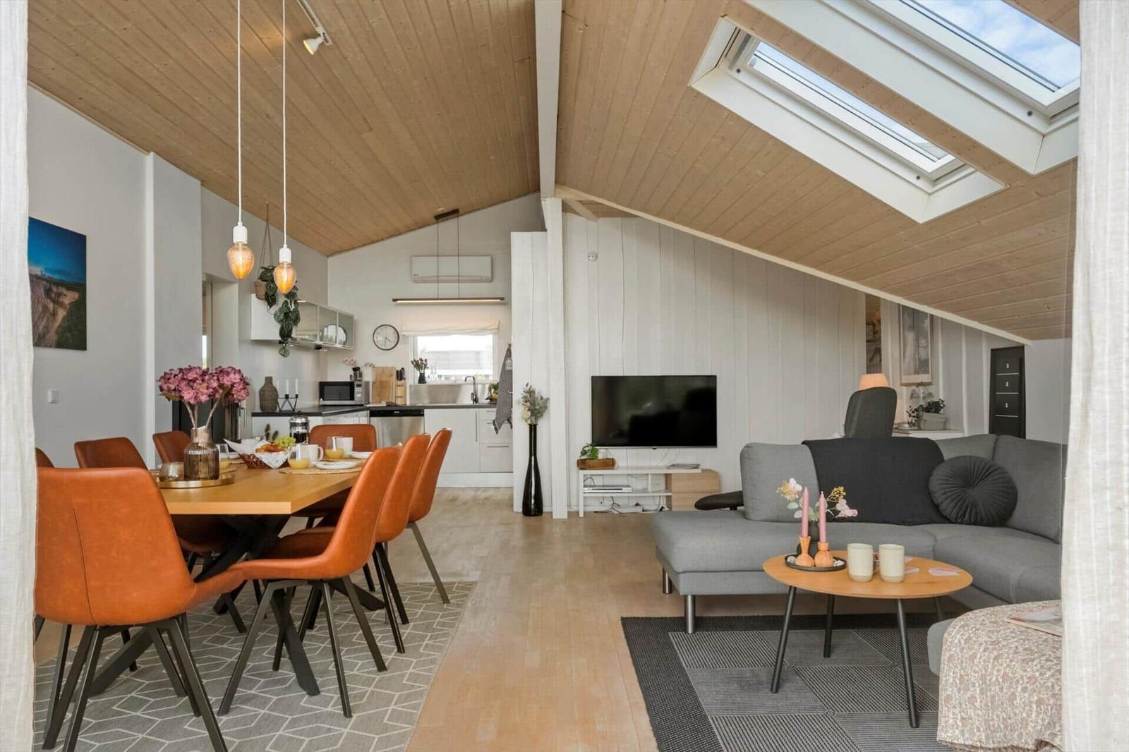 Wohn- und Essbereich mit Holzdecke, Sofa, Esstisch und Küchenbereich.