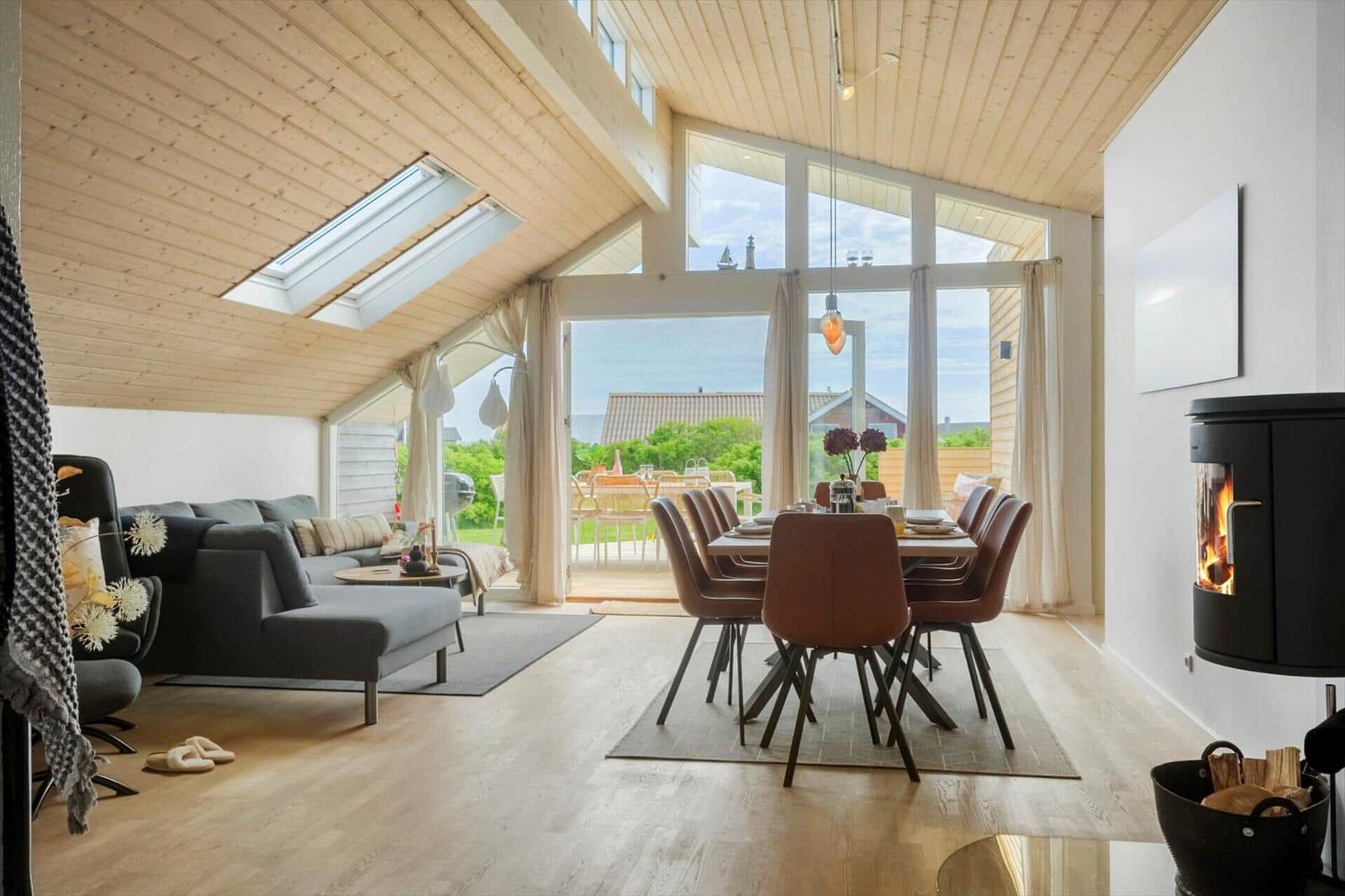 Wohn- und Essbereich mit Holzdecke, großem Fenster und Kaminofen.