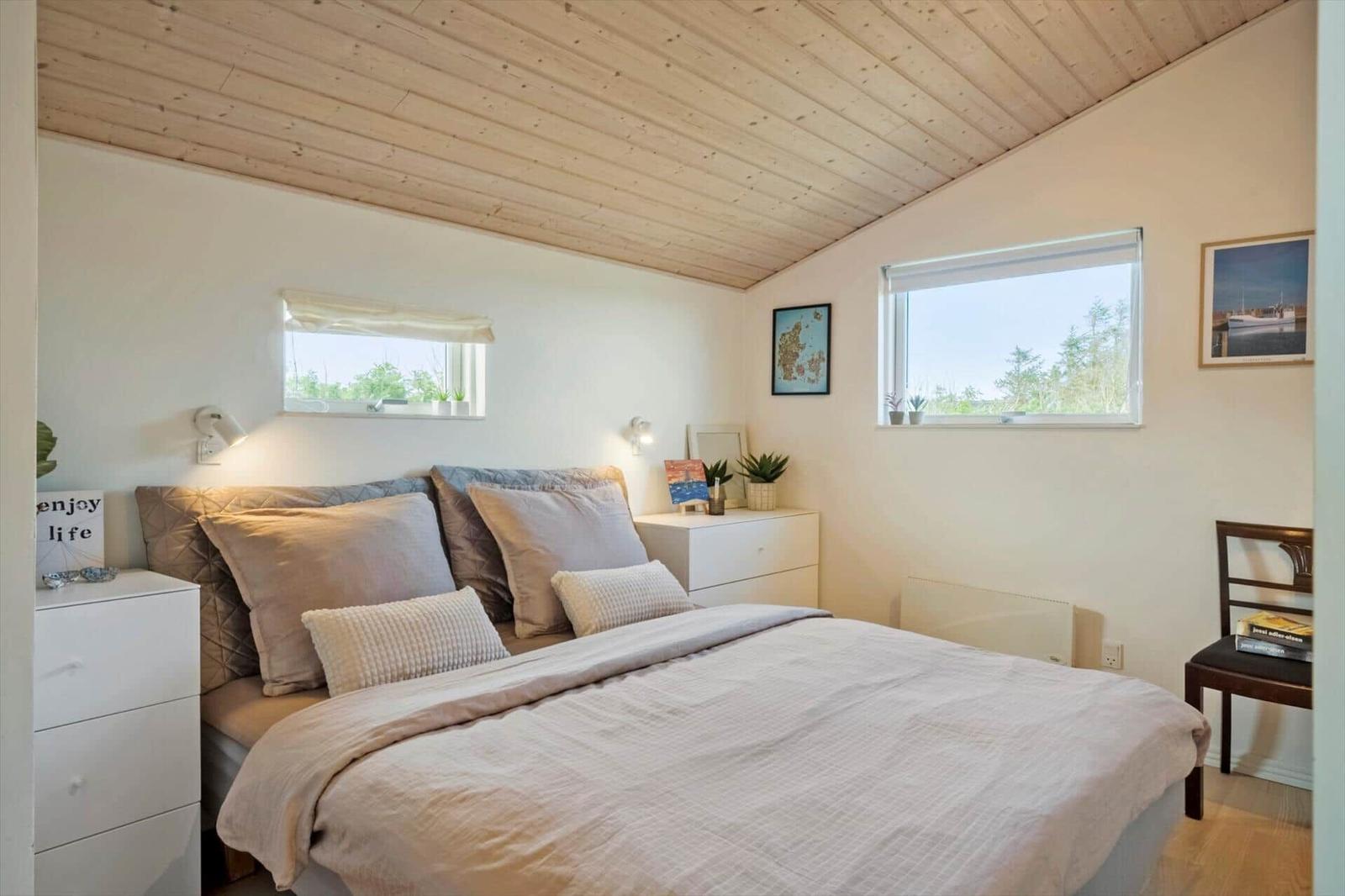 Schlafzimmer mit Bett, zwei Fenstern und weißen Schränken.