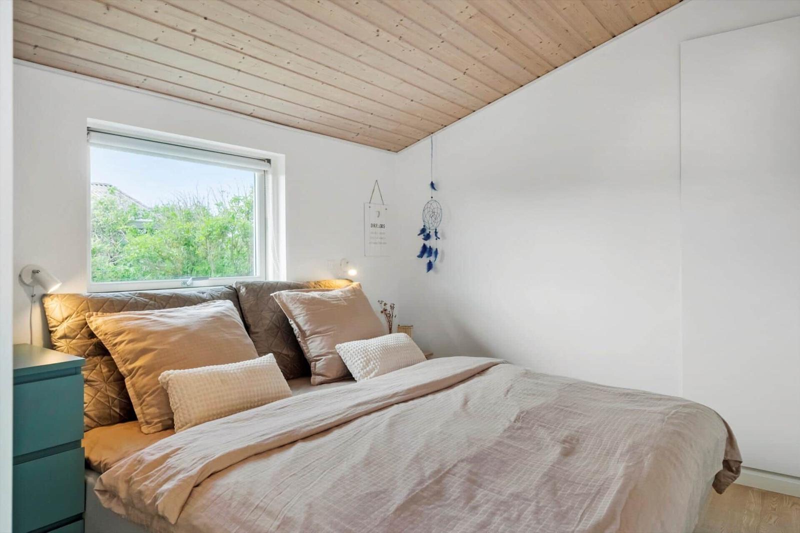 Schlafzimmer mit Bett, Fenster und Holzdecke.