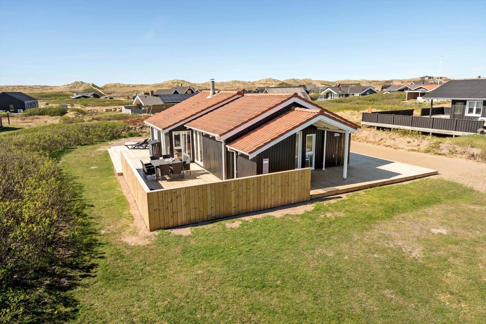 Holzhaus mit Terrasse und Garten. Hintergrund: Dünen und weitere Häuser.