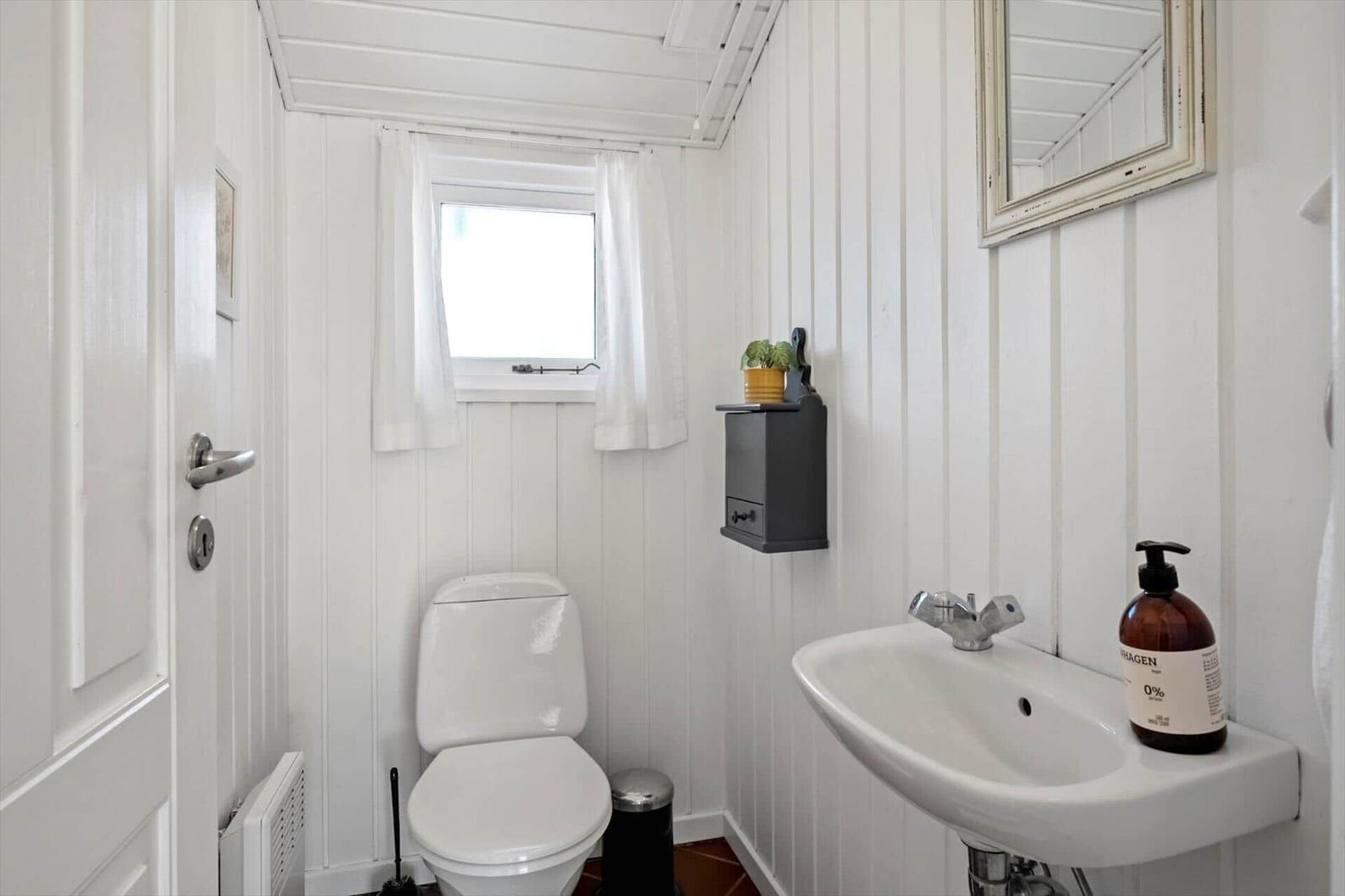 Badezimmer mit Toilette, Waschbecken und Fenster. Weiße Wände und Holzpaneelen.