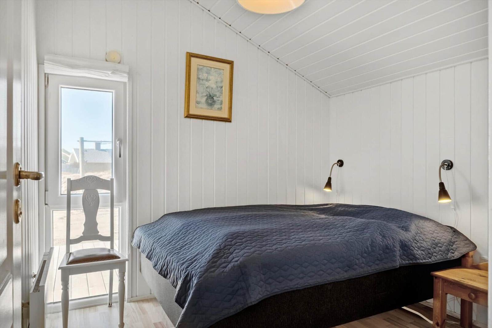 Schlafzimmer mit Bett, Wandlampen und Tür zum Balkon.