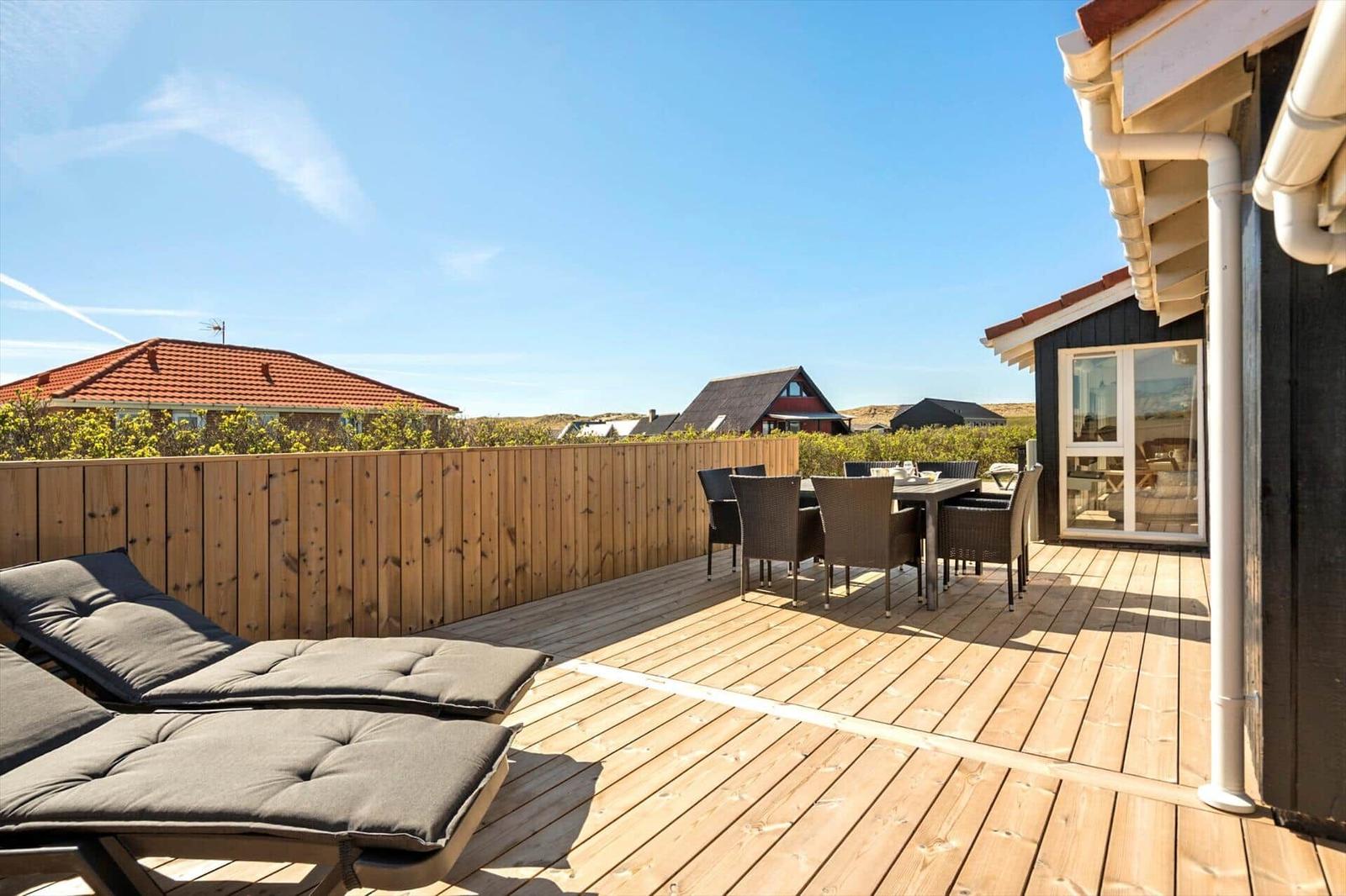 Terrasse mit Liegestühlen und Esstisch. Holzgeländer und Blick auf Häuser.