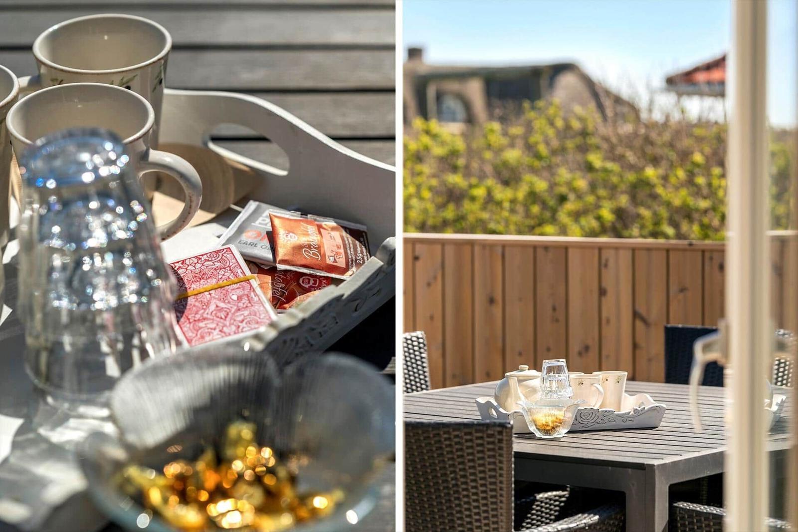 Terrasse mit Tisch, Stühlen und Teezubehör. Hintergrund: Holzgeländer und grüne Pflanzen.