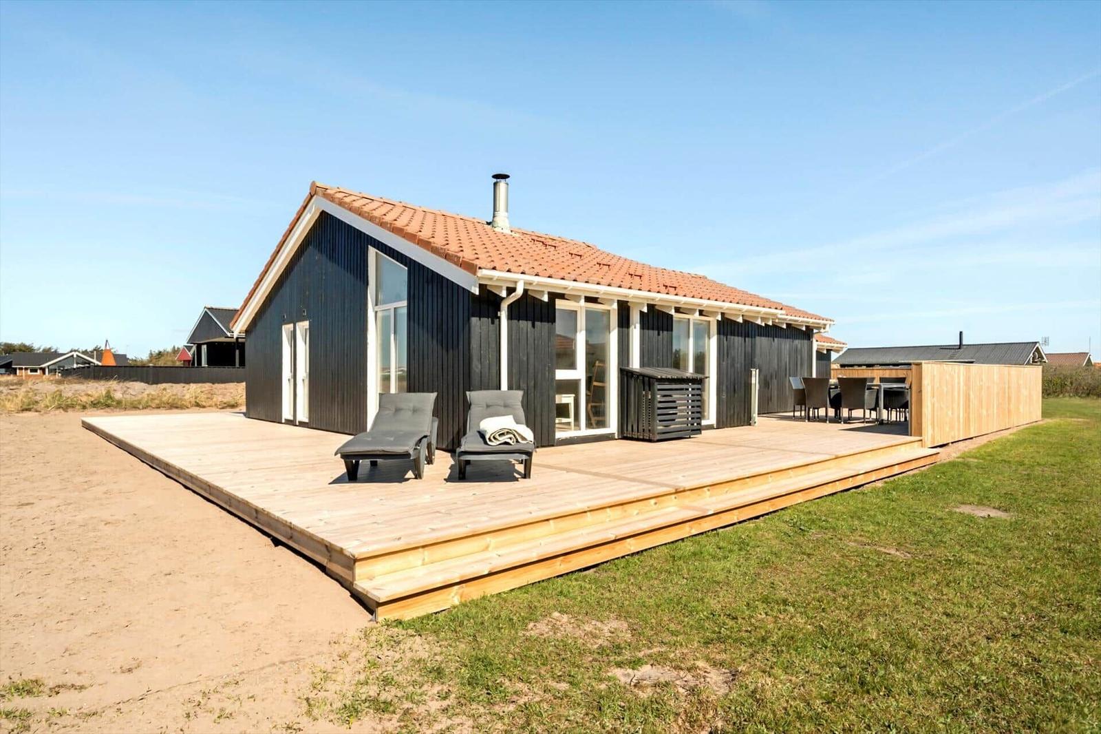 Moderne Strandhaus mit Holzterrasse, Liegestühlen und Garten.