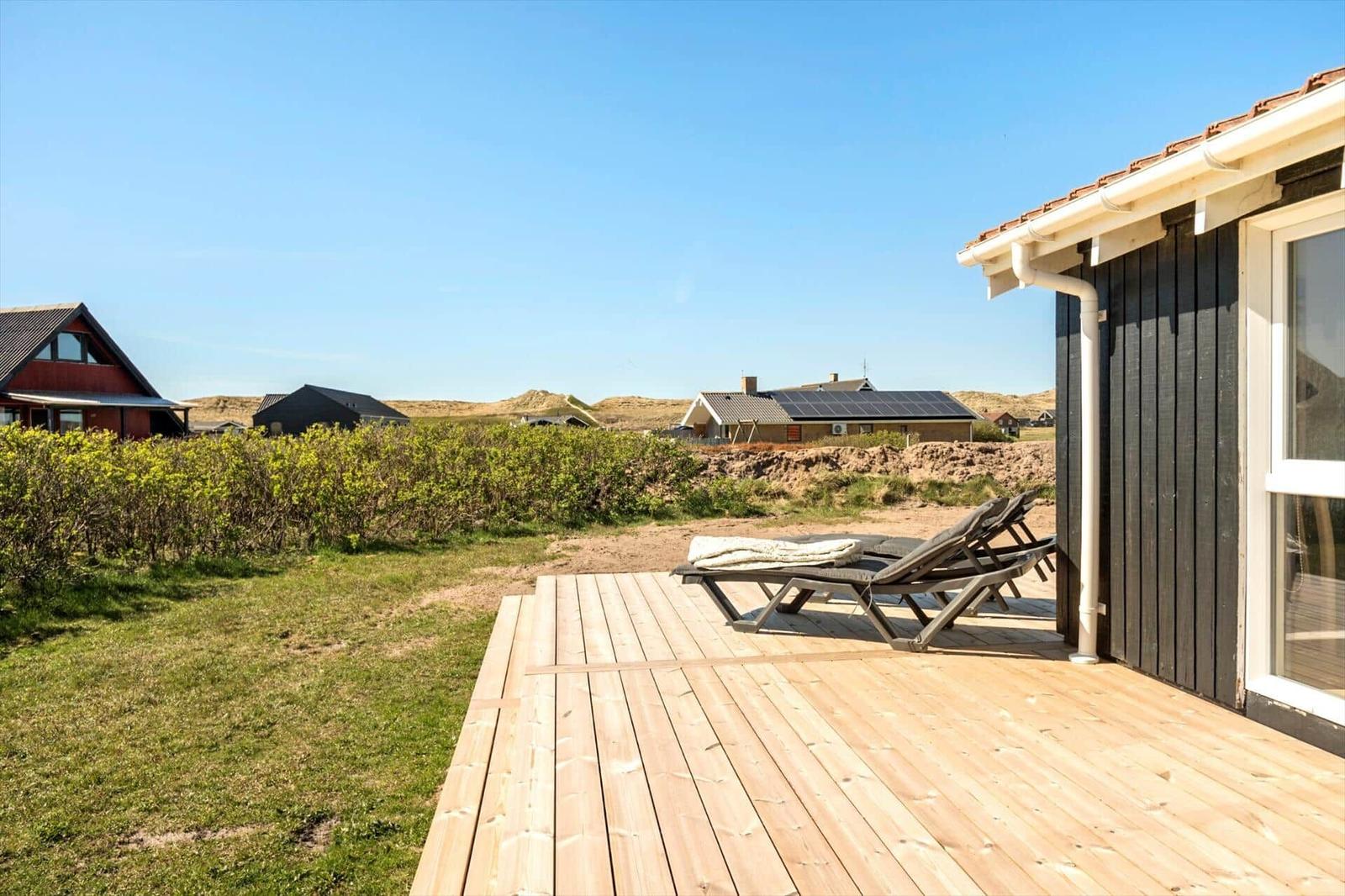 Terrasse mit Liegestühlen neben einem Haus. Im Hintergrund sind weitere Häuser und Dünen zu sehen.