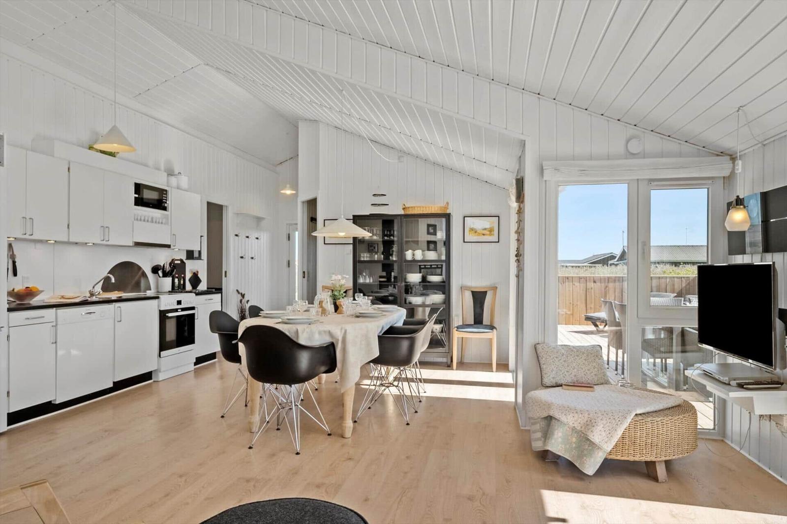 Wohnküche mit Esstisch, TV und Terrasse. Weiße Wände, Holzboden und Glasfront.