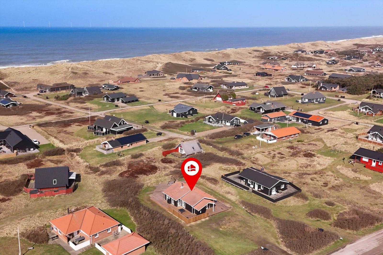 Haus mit rotem Dach in Strandnähe, umgeben von Wiesen und anderen Häusern.