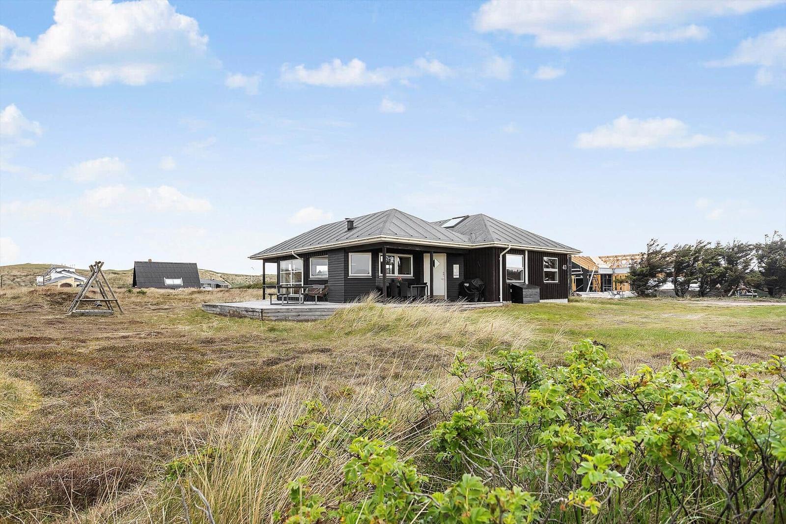 Ein modernes Haus mit Terrasse in einer grasbewachsenen Landschaft unter blauem Himmel.