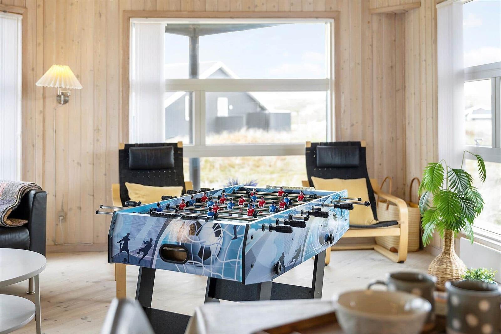 Ein Foosballtisch steht im Wohnzimmer mit Holzwänden und großen Fenstern.