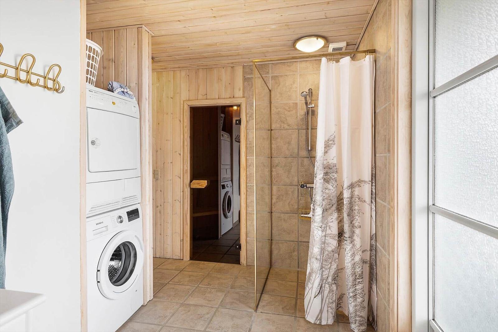 Dusche mit Duschvorhang, Waschmaschine und Trockner in Holzvertäfelung