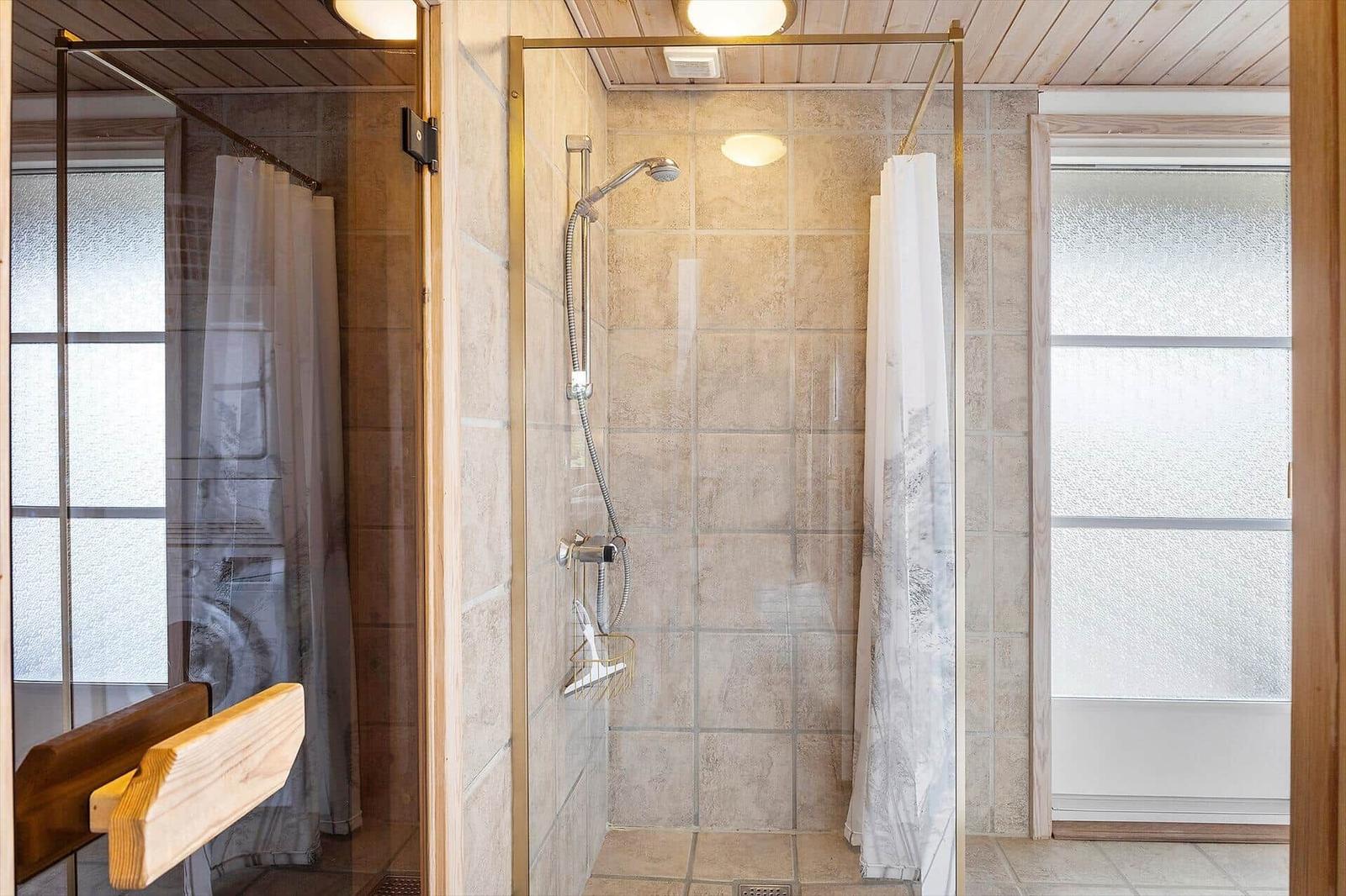 Dusche mit Glaswand, Duschbrause und gefliesten Wänden. Fenster mit Milchglas.