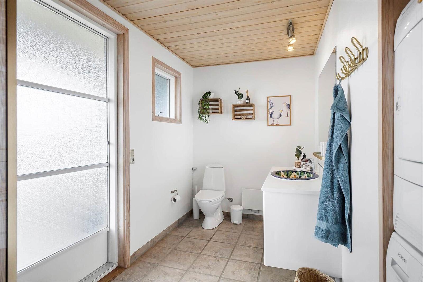 Badezimmer mit Toilette, Waschbecken und Badewanne. Holzdecke und Fenster mit Milchglas.