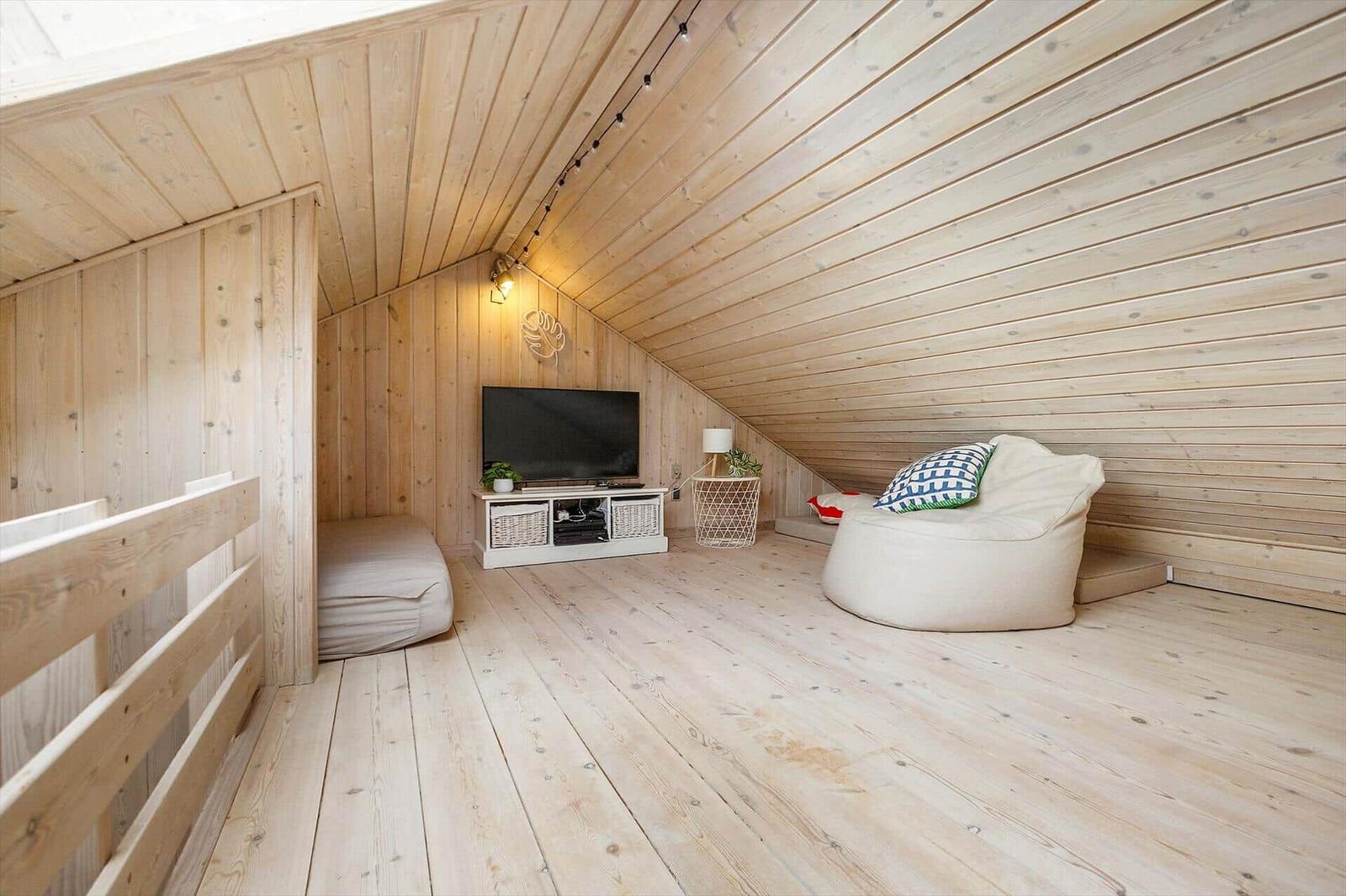 Dachgeschosszimmer mit Holzwand, TV, Sitzgelegenheit und Deckenleuchte.