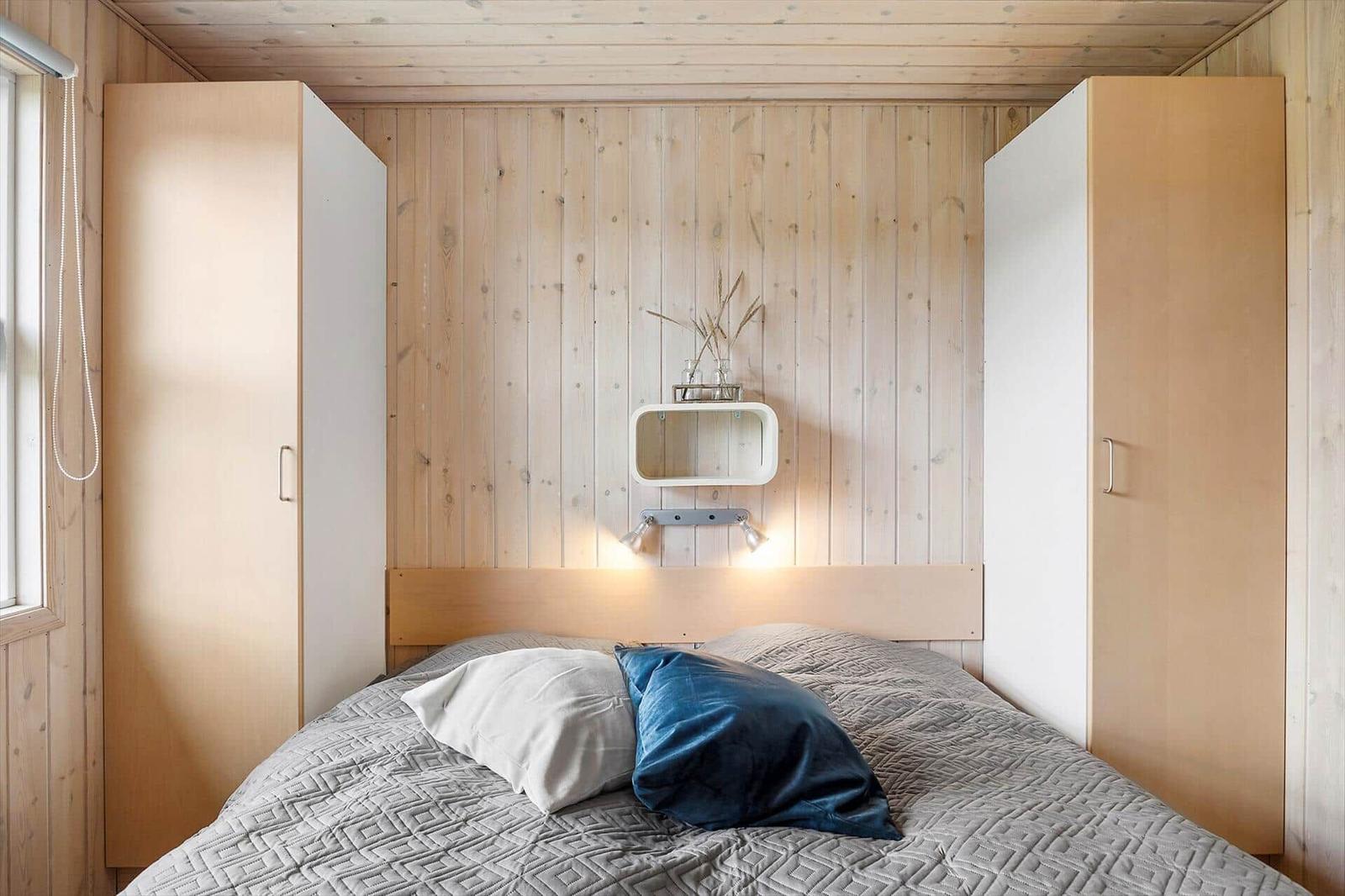 Schlafzimmer mit Bett, Holzwand und weißen Schränken. Wandregal mit Pflanzen und Beleuchtung.