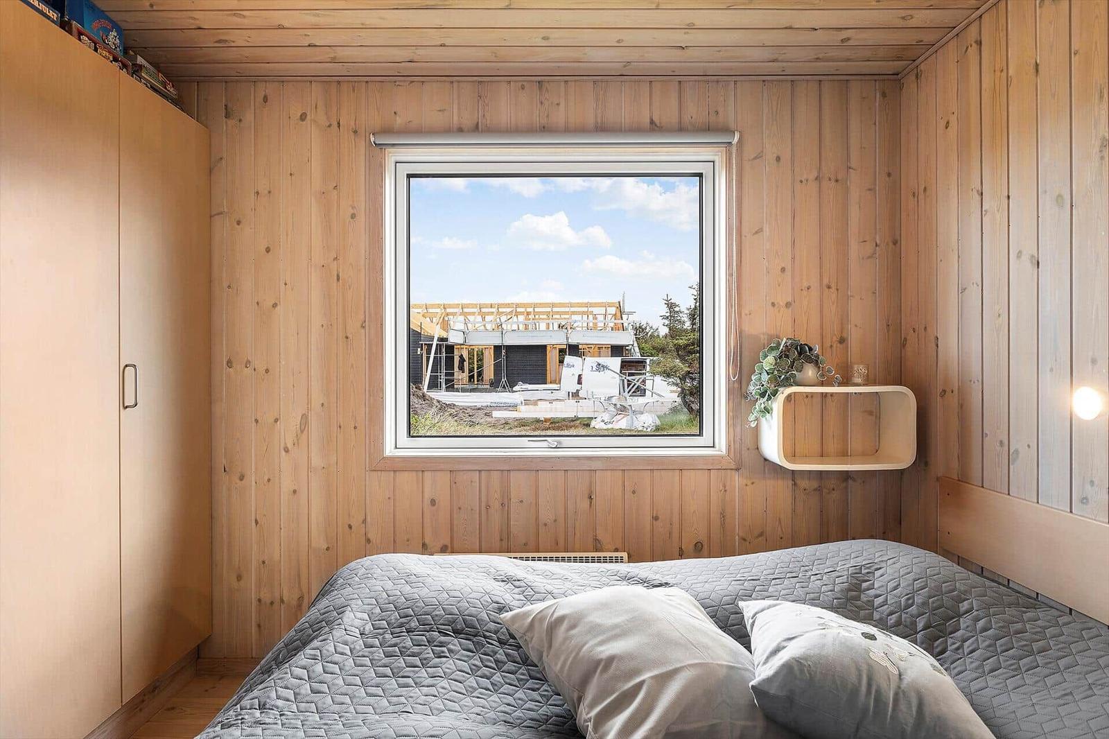 Schlafzimmer mit Holzwand, Bett und Fensterblick auf Baustelle.