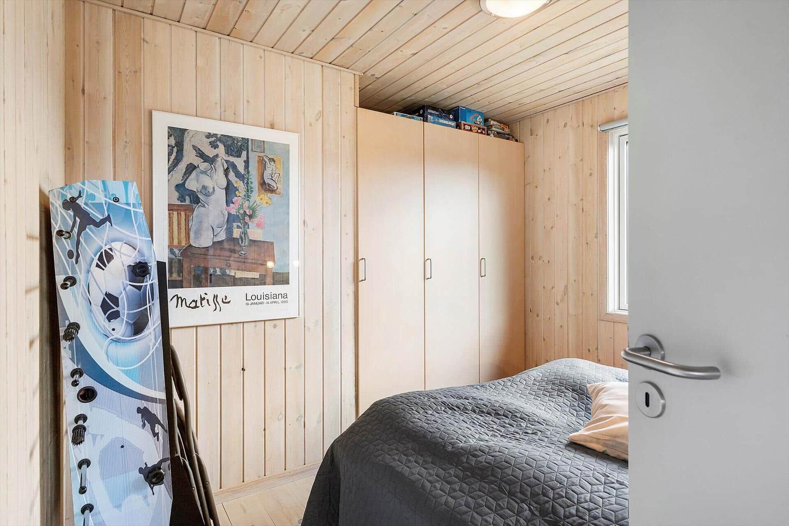 Schlafzimmer mit Holzwand, Bett, Kleiderschrank und Wandbild.