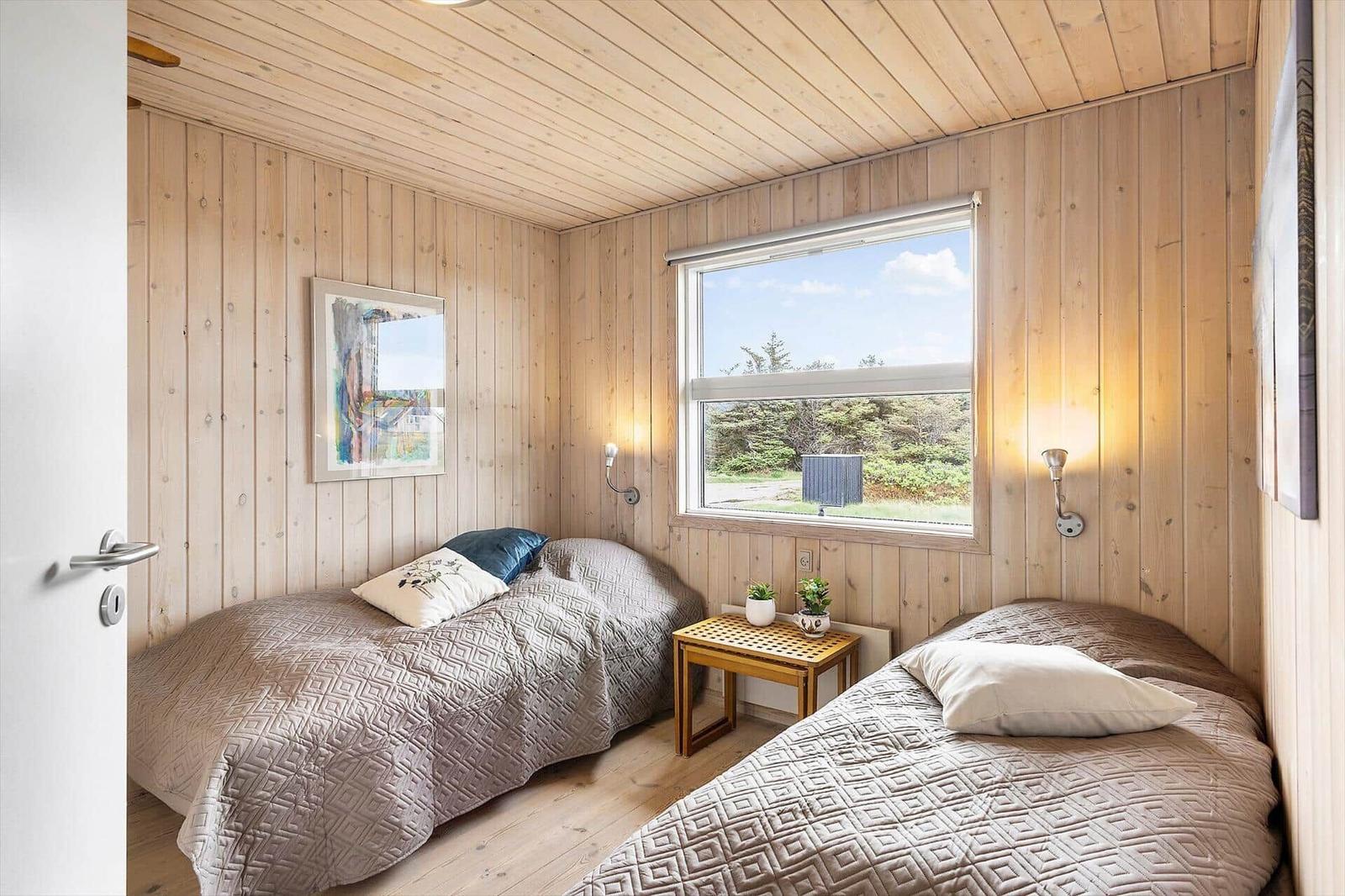 Zwei Betten in einem Zimmer mit Holzwänden und Fensterblick auf Grünflächen.