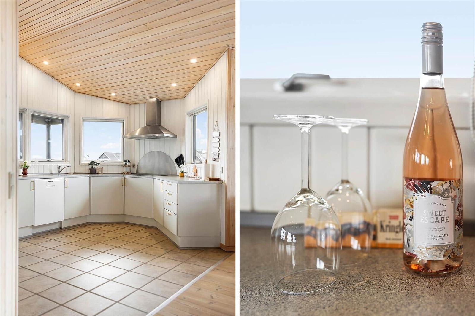 Küche mit Holzdecke und weißen Schränken. Weinflasche und Gläser auf Arbeitsfläche.