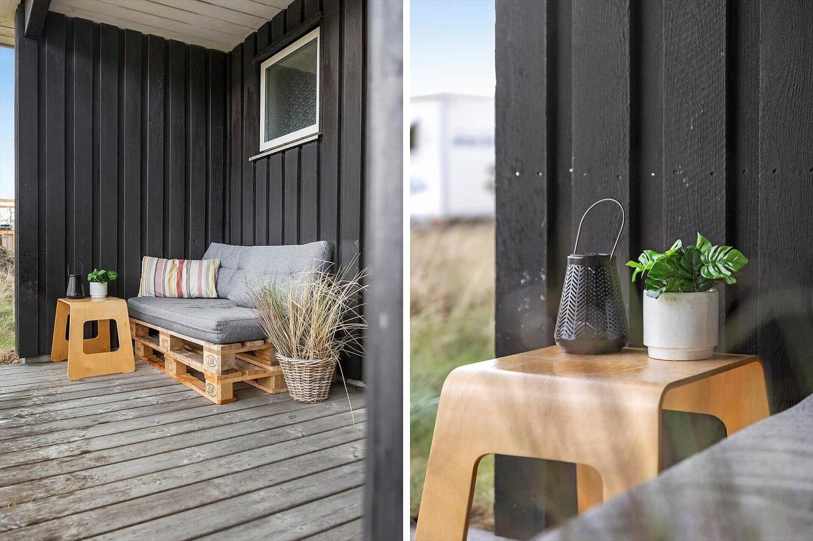 Terrasse mit Sitzbank aus Paletten, Holztisch und Pflanzen vor schwarzem Holzhaus.