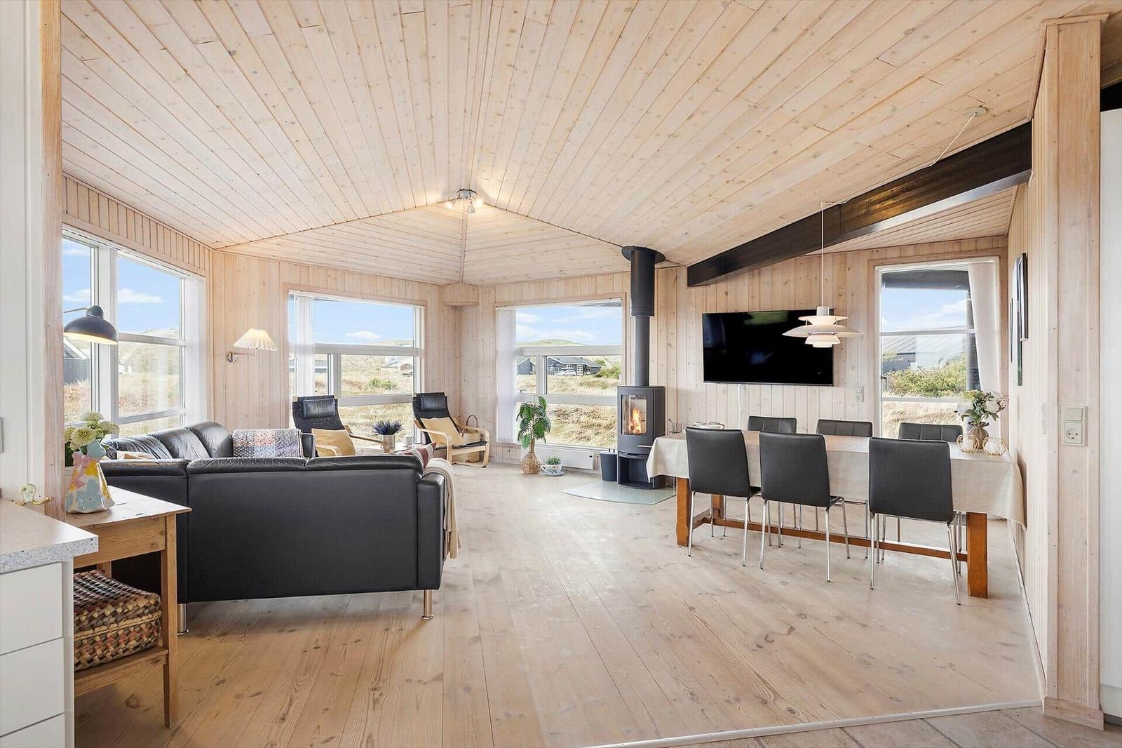 Wohn- und Essbereich mit Holzdecke, Kamin und großen Fenstern.