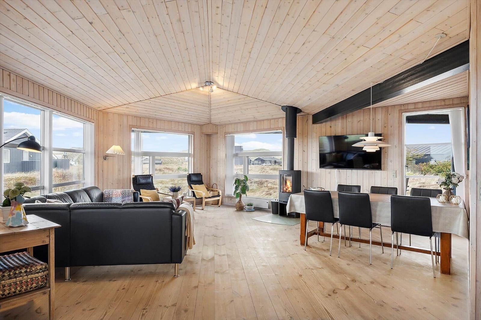 Wohn- und Essbereich mit Holzdecke, Kamin und großen Fenstern.