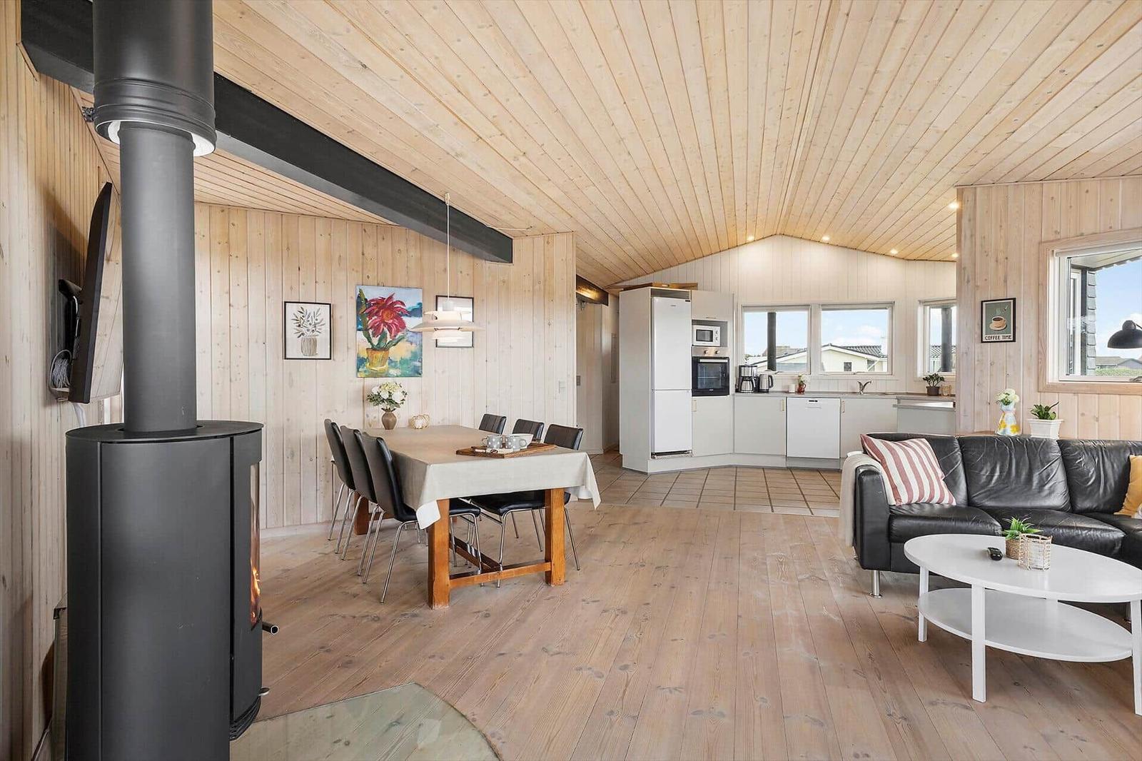Wohnküche mit Holzdecke, Esstisch, Sofa und Kaminofen.