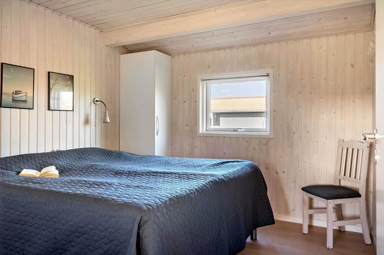 Schlafzimmer mit Bett, Stuhl und Fenster. Wände aus Holz, Bilder an der Wand.