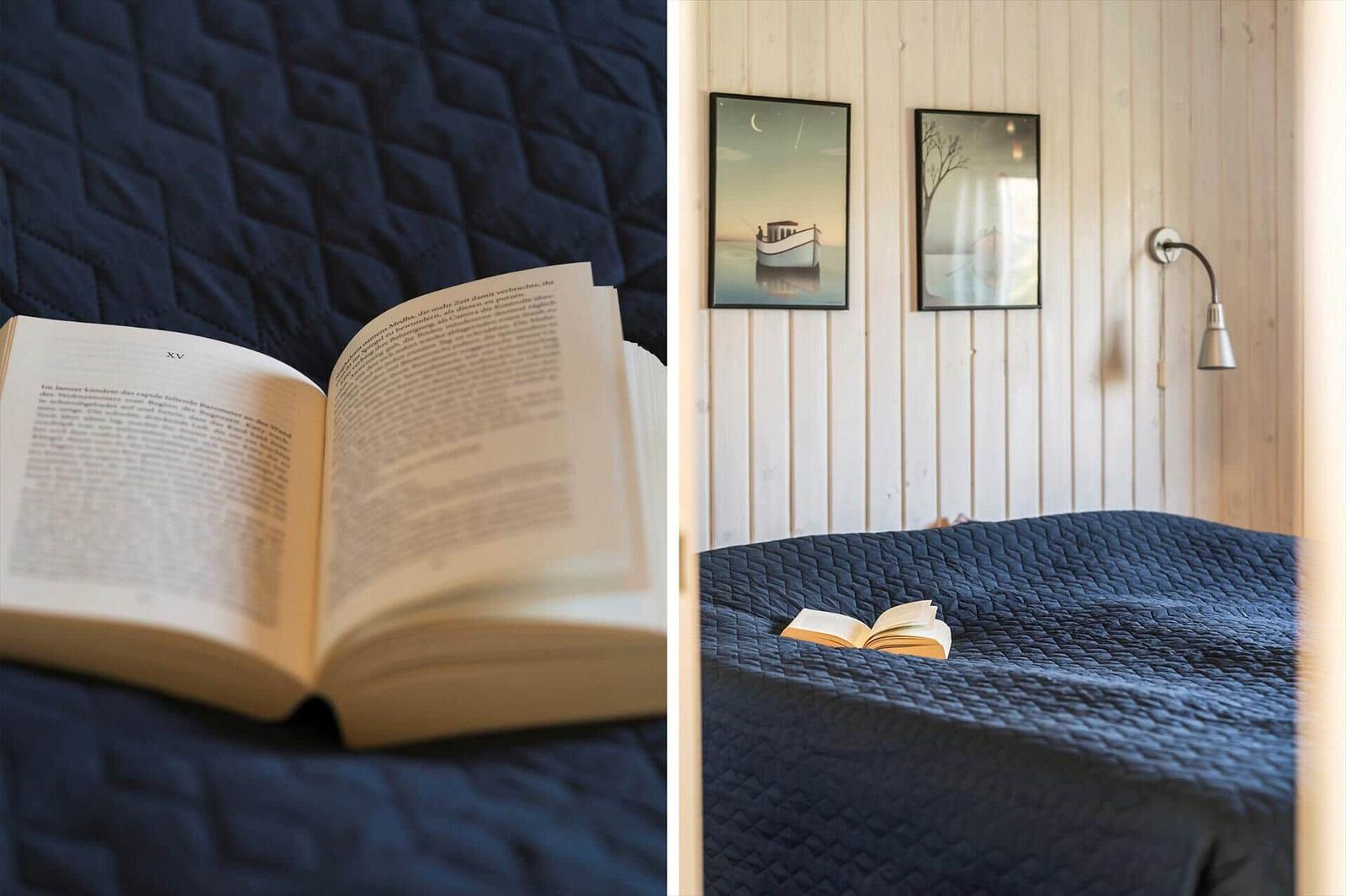 Ein Buch liegt auf einem Bett mit dunkelblauer Decke. An der Wand hängen zwei Bilder.