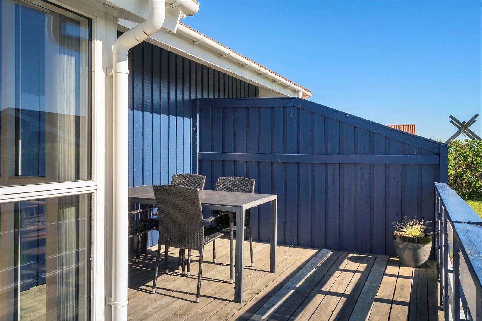 Terrasse mit Tisch und Stühlen, blauer Holzaufbau und Pflanze