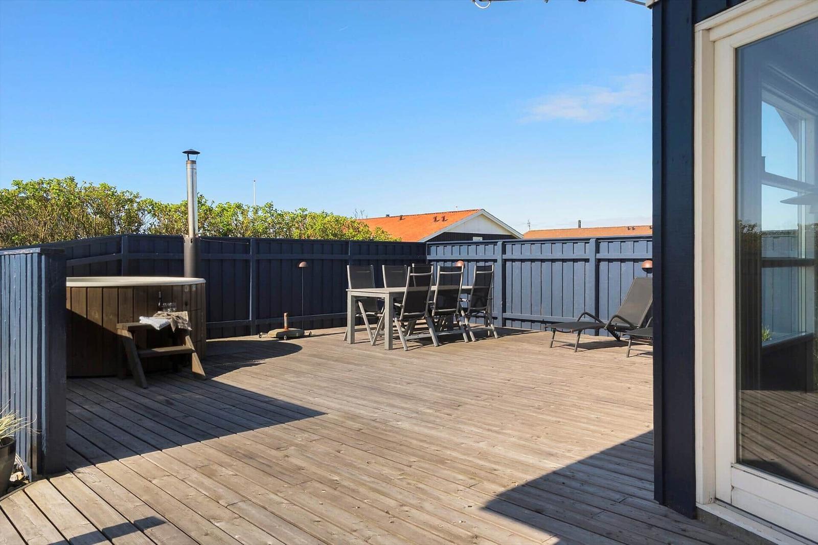 Terrasse mit Holzboden, Sitzgruppe, Liegestühlen und Whirlpool. Umzäunt mit dunkelblauem Holzzaun.