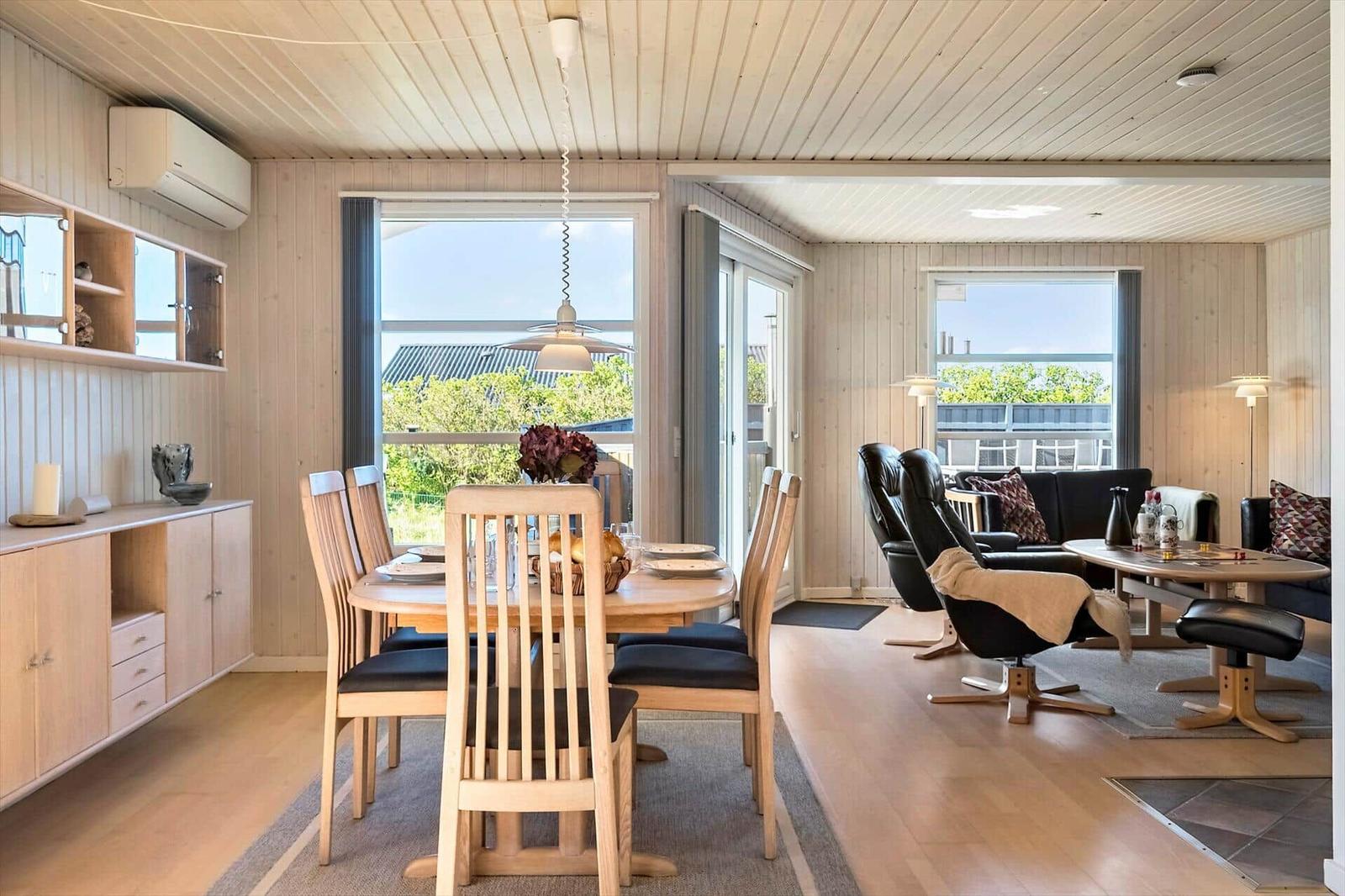 Essbereich mit Tisch und Stühlen. Wohnbereich mit Sofa und Sessel. Holzwände und Boden.