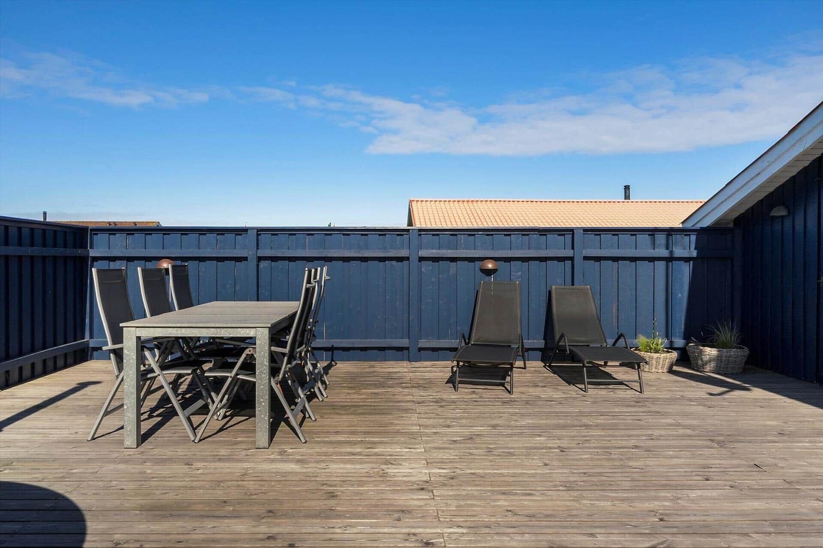 Terrasse mit Tisch, Stühlen und Liegestühlen. Holzdecke und blaue Umzäunung.