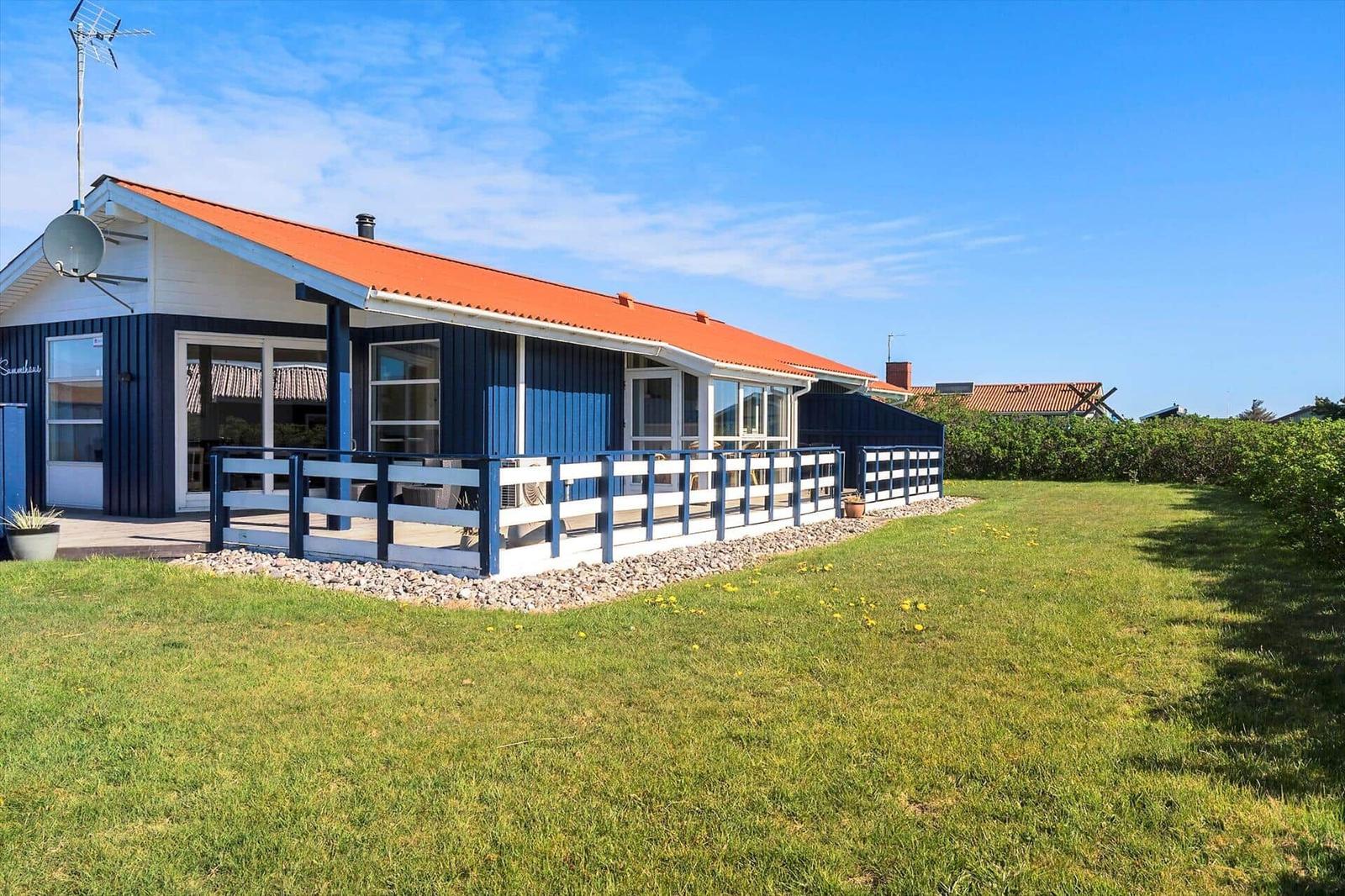 Ein Haus mit blauem Holzschindelgehäuse und rotem Dach. Vorne befindet sich eine Terrasse mit weiß-blauer Brüstung.