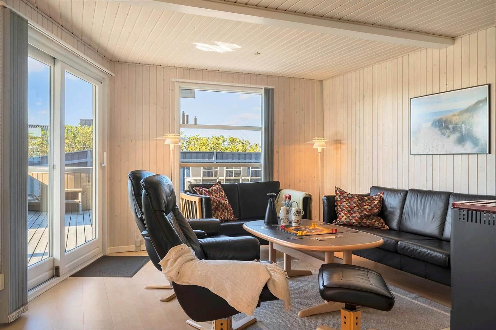 Wohnzimmer mit schwarzen Ledersofas, Holztisch und Blick auf Balkon.