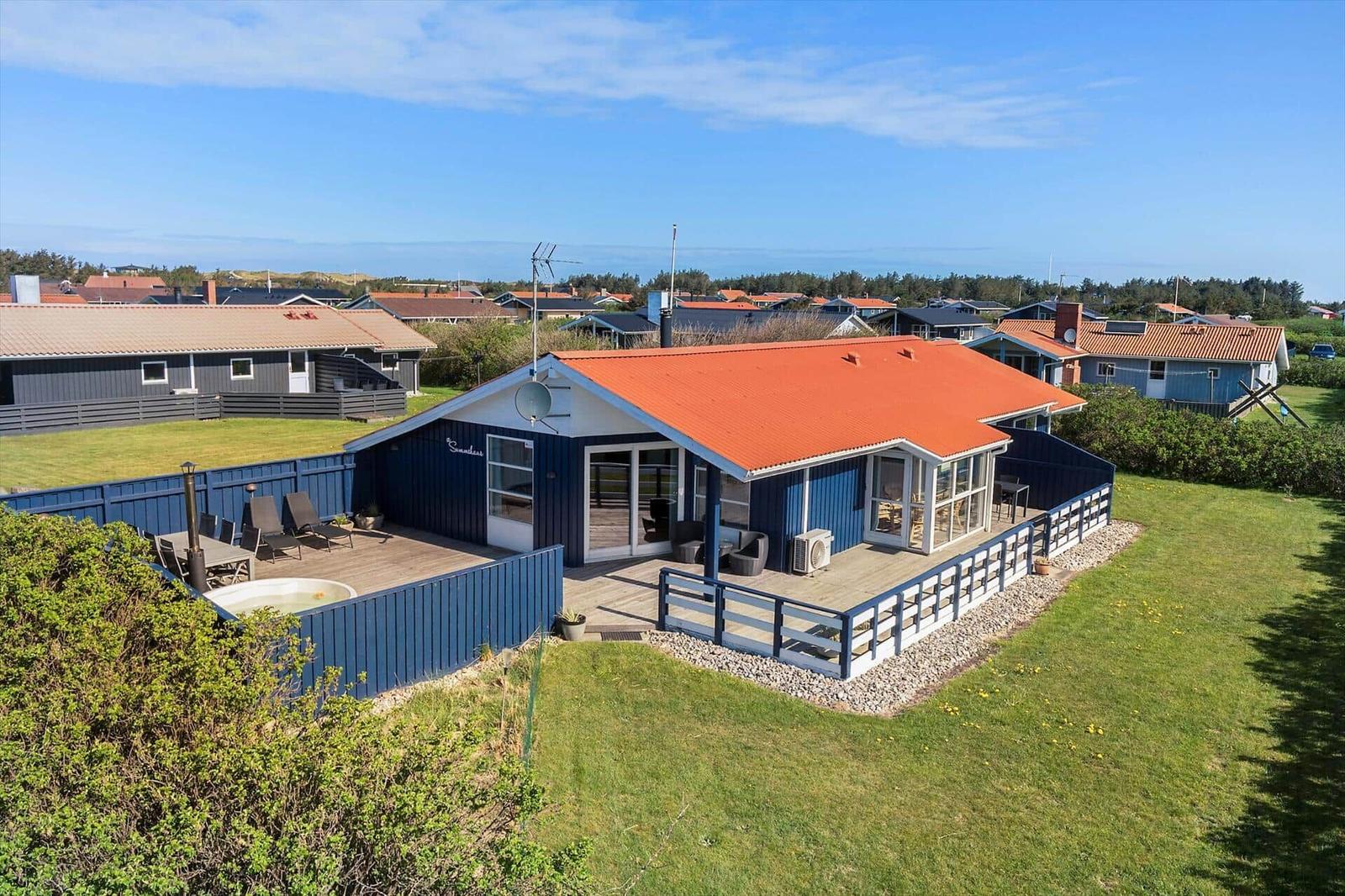 Ein Haus mit rotem Dach und blauen Wänden hat eine große Terrasse mit Gartenmöbeln und einen Whirlpool.