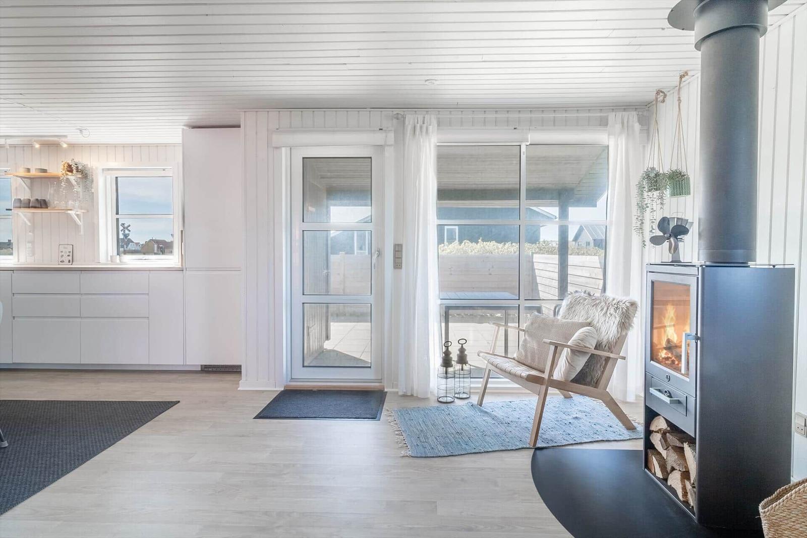 Wohnraum mit Kamin, Sessel und Blick auf Terrasse.