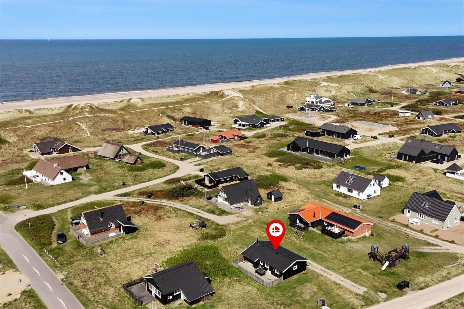 Strandnahe Ferienhäuser in einer Dünenlandschaft mit Blick aufs Meer.