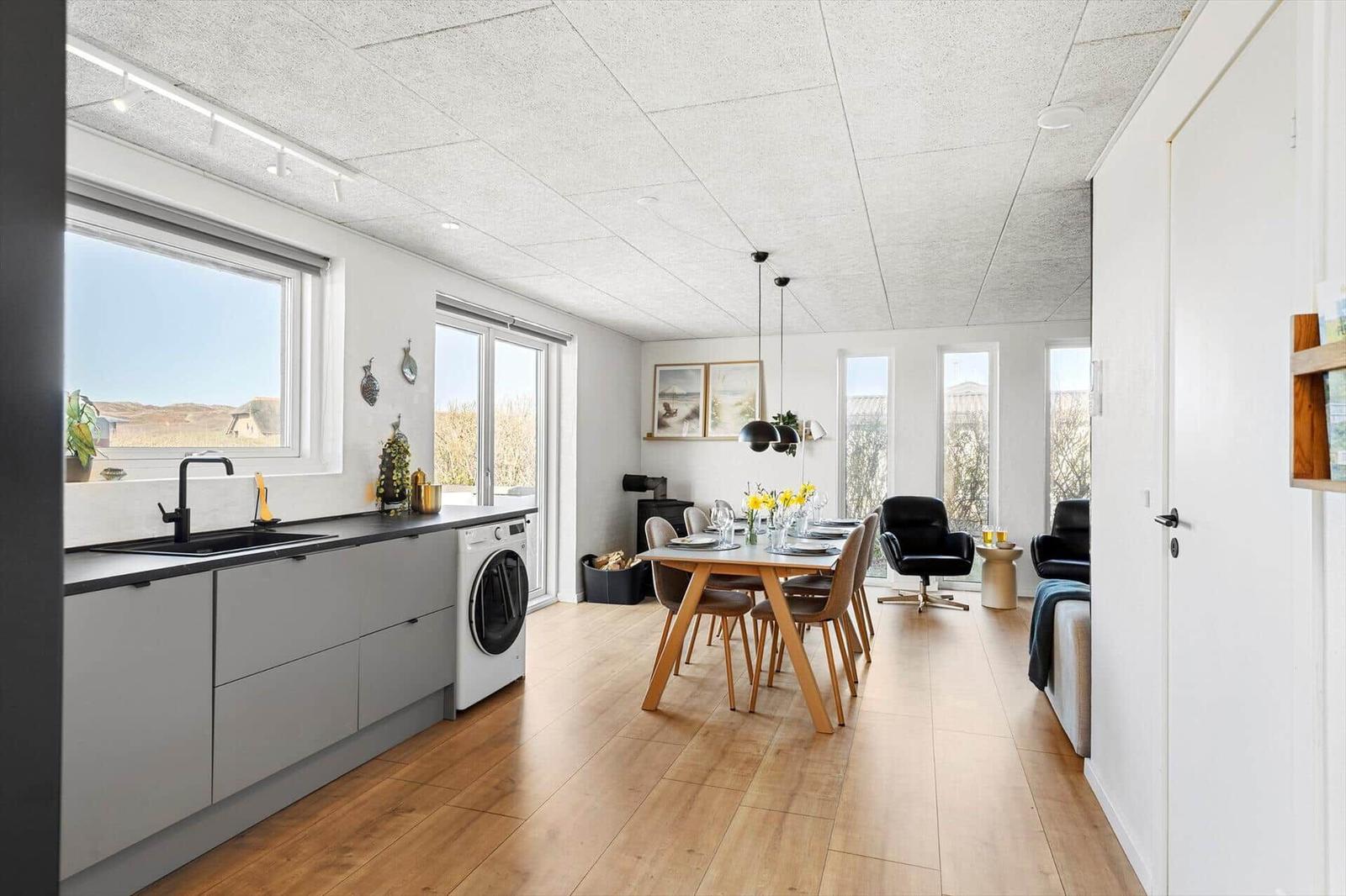 Küche mit Waschmaschine, Essbereich mit Tisch und Stühlen, Fenster mit Blick auf Landschaft.