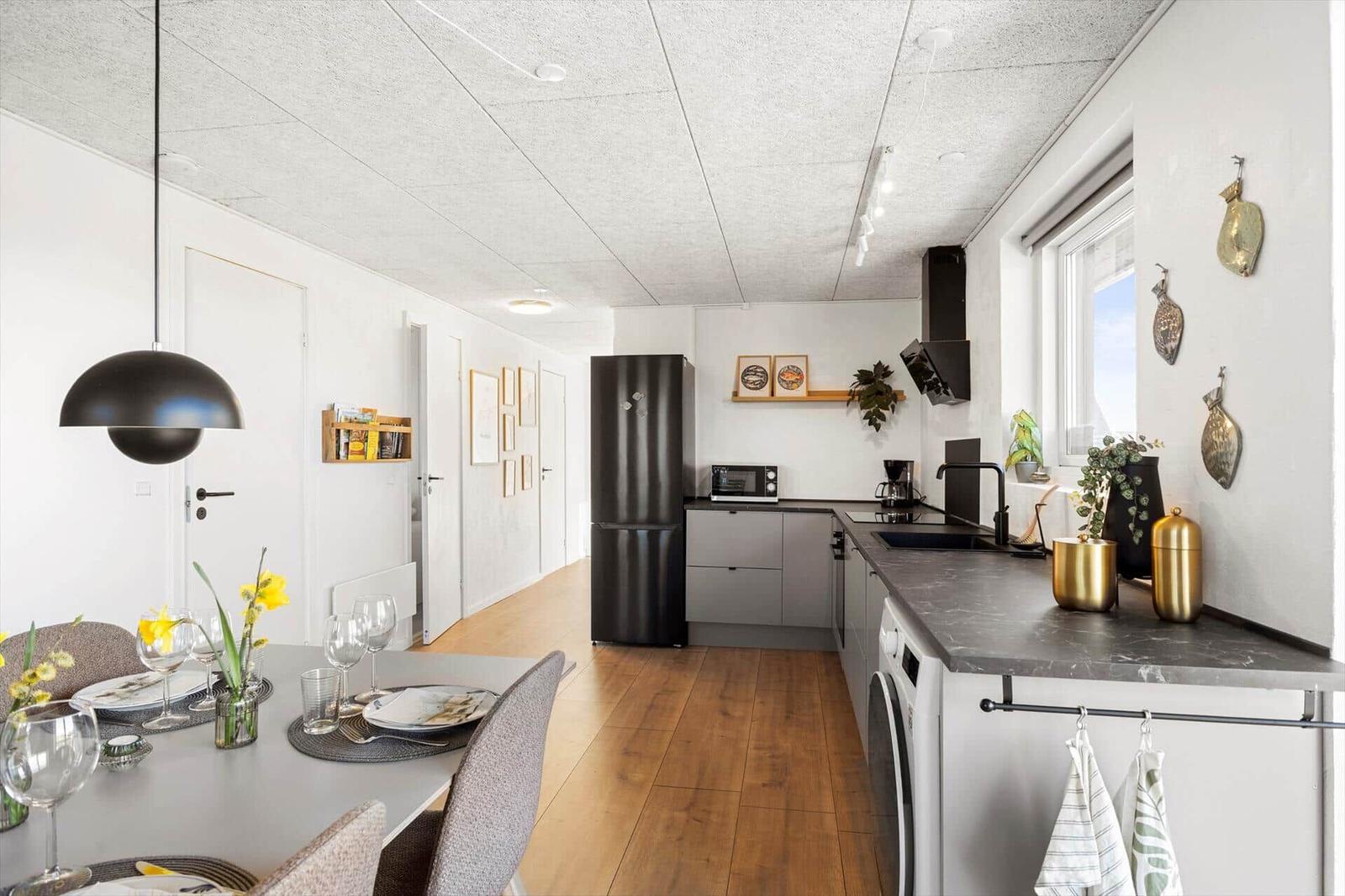 Küche mit Esstisch, schwarzer Kühlschrank und Holzboden.