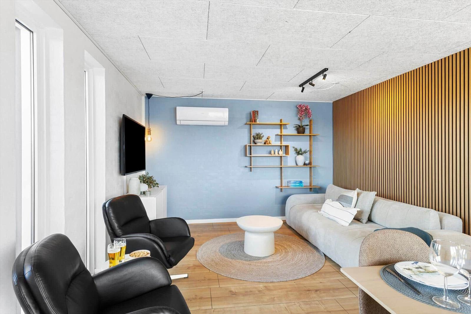 Wohnzimmer mit Sofa, zwei Sesseln, runden Tisch und Holzboden.