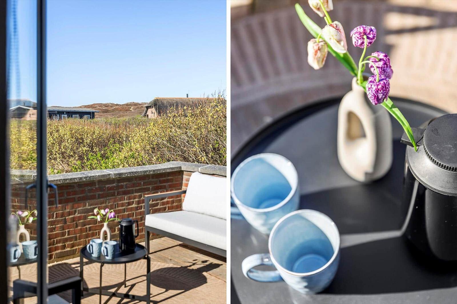 Terrasse mit Sitzgelegenheit und Blick auf Landschaft. Tisch mit Tassen und Blumen.