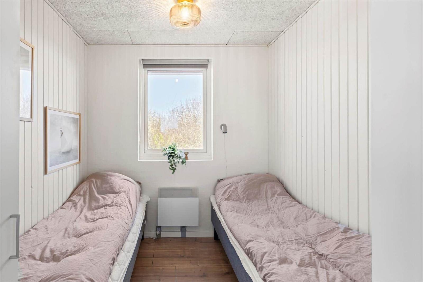 Zwei Betten mit rosa Bettwäsche, Fenster und Heizkörper in einem Raum mit weißen Wänden.