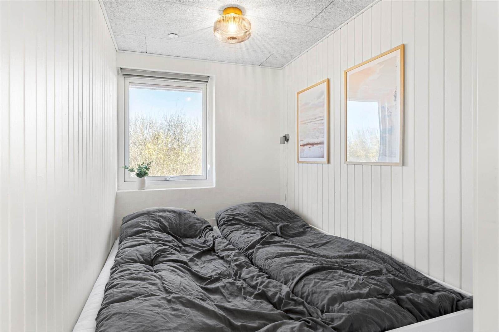 Schlafzimmer mit Bett, Fenster und Wandbildern.