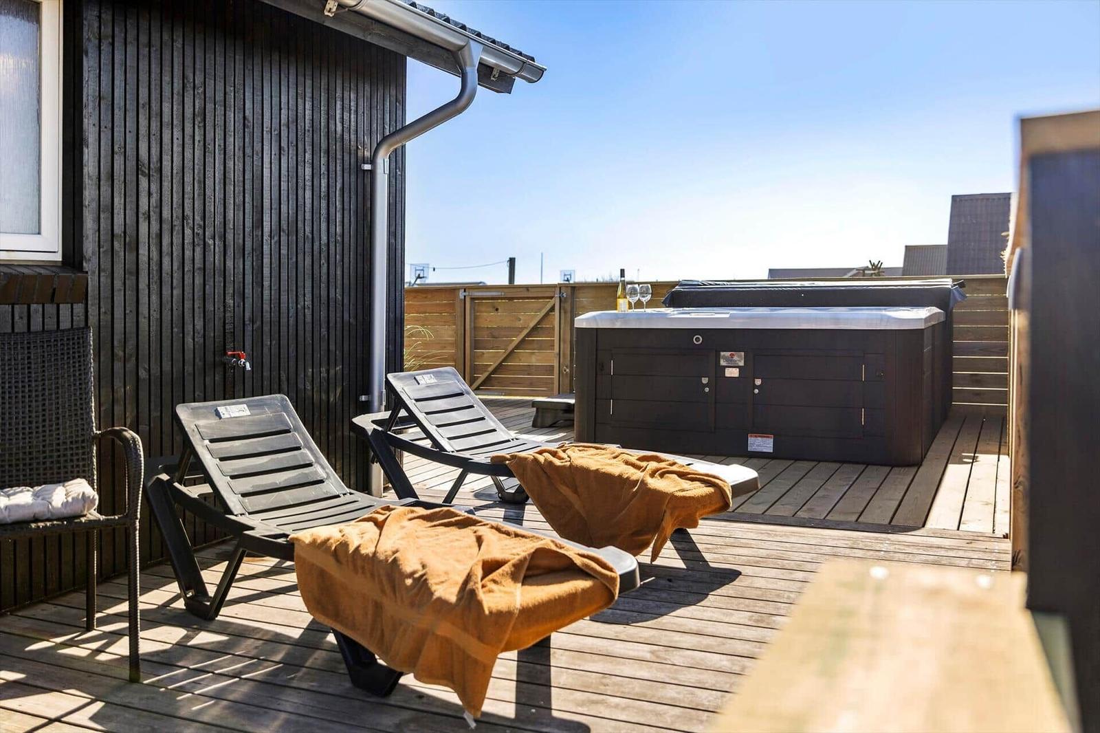 Terrasse mit Liegestühlen, Whirlpool und Holzdecke. Hintergrund: Holzzaun und klare Himmel.