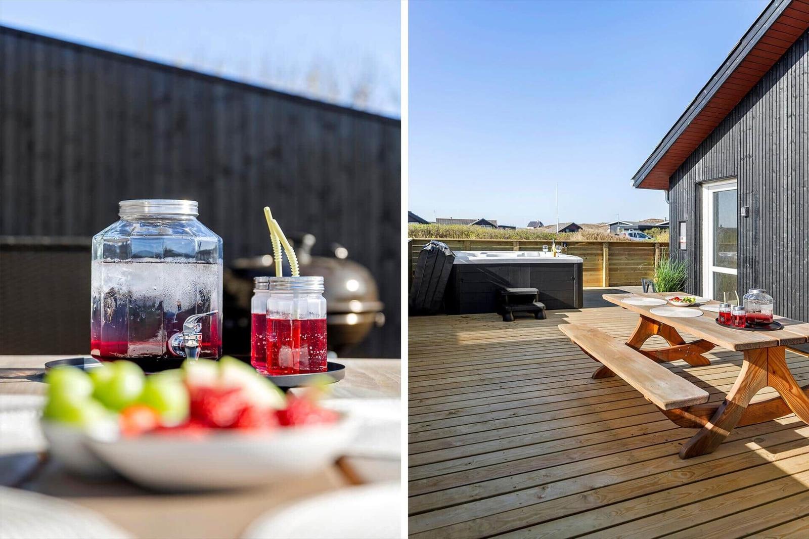 Terrasse mit Holztisch, Whirlpool und Grillbereich. Getränke und Obst auf dem Tisch.