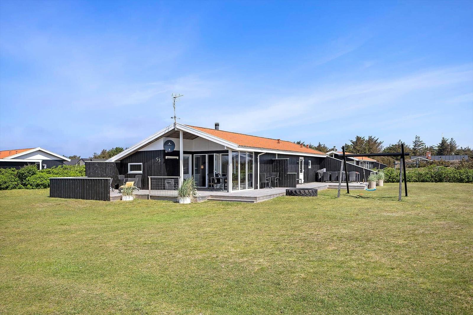 Moderne Ferienhaus mit Terrasse und Garten. Schwarze Holzwand, orangefarbener Dachfirst.