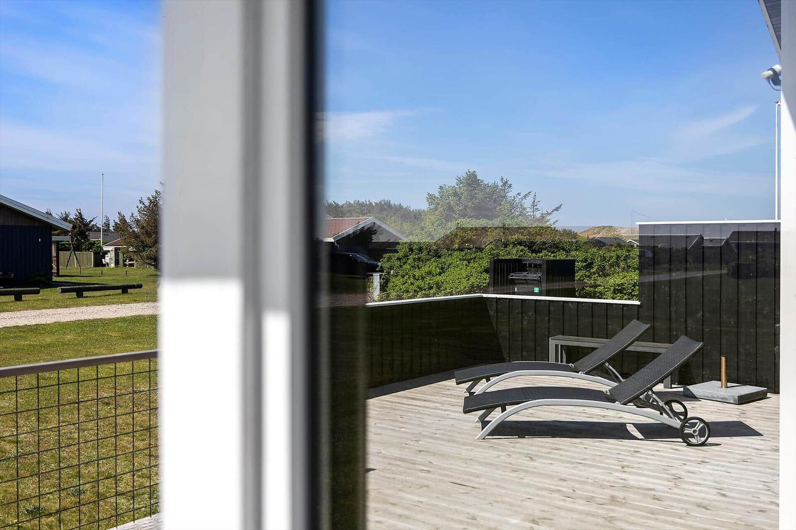Terrasse mit zwei Liegestühlen, Holzboden und Blick auf Grünfläche und Bäume.